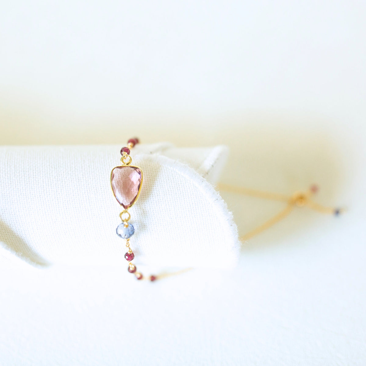 Pink gemstone Isla bracelet with gold-tone links and small bead accents on a white display.