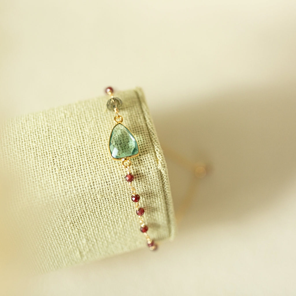 Pale green gemstone Isla bracelet with gold-tone links on a fabric display.