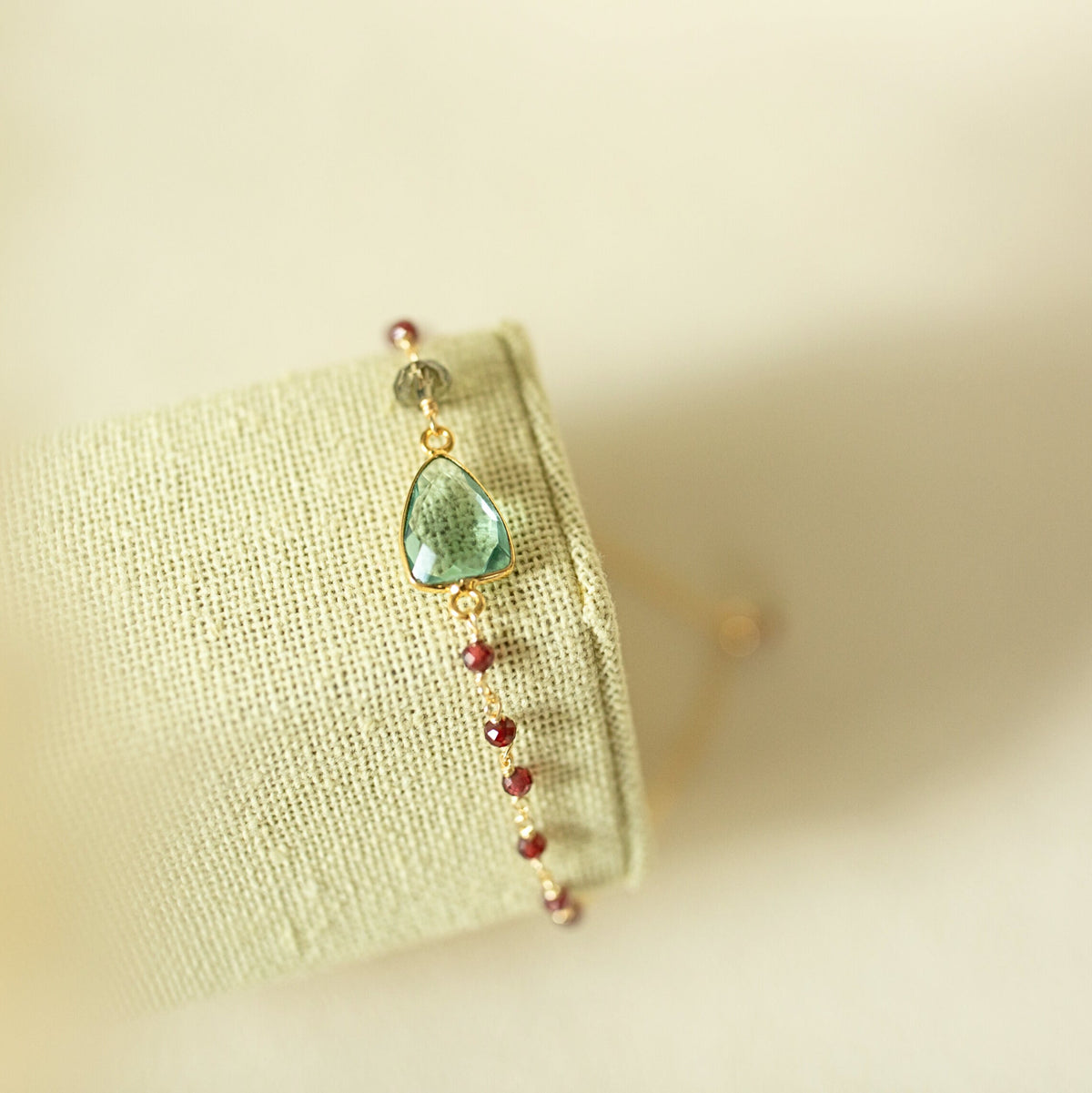 Pale green gemstone Isla bracelet with gold-tone links on a fabric display.