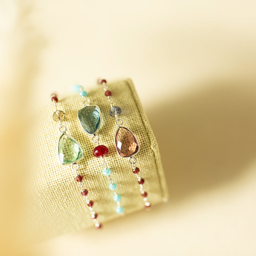Three Isla bracelets with green, blue and pink gemstones on a fabric display.