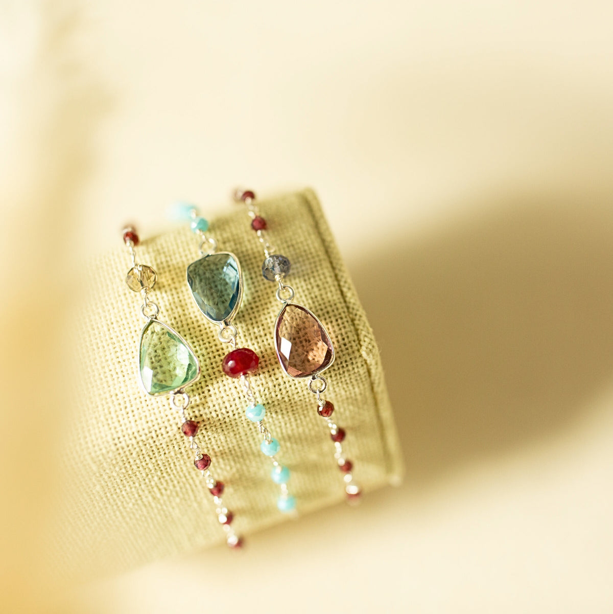 Three Isla bracelets with green, blue and pink gemstones on a fabric display.
