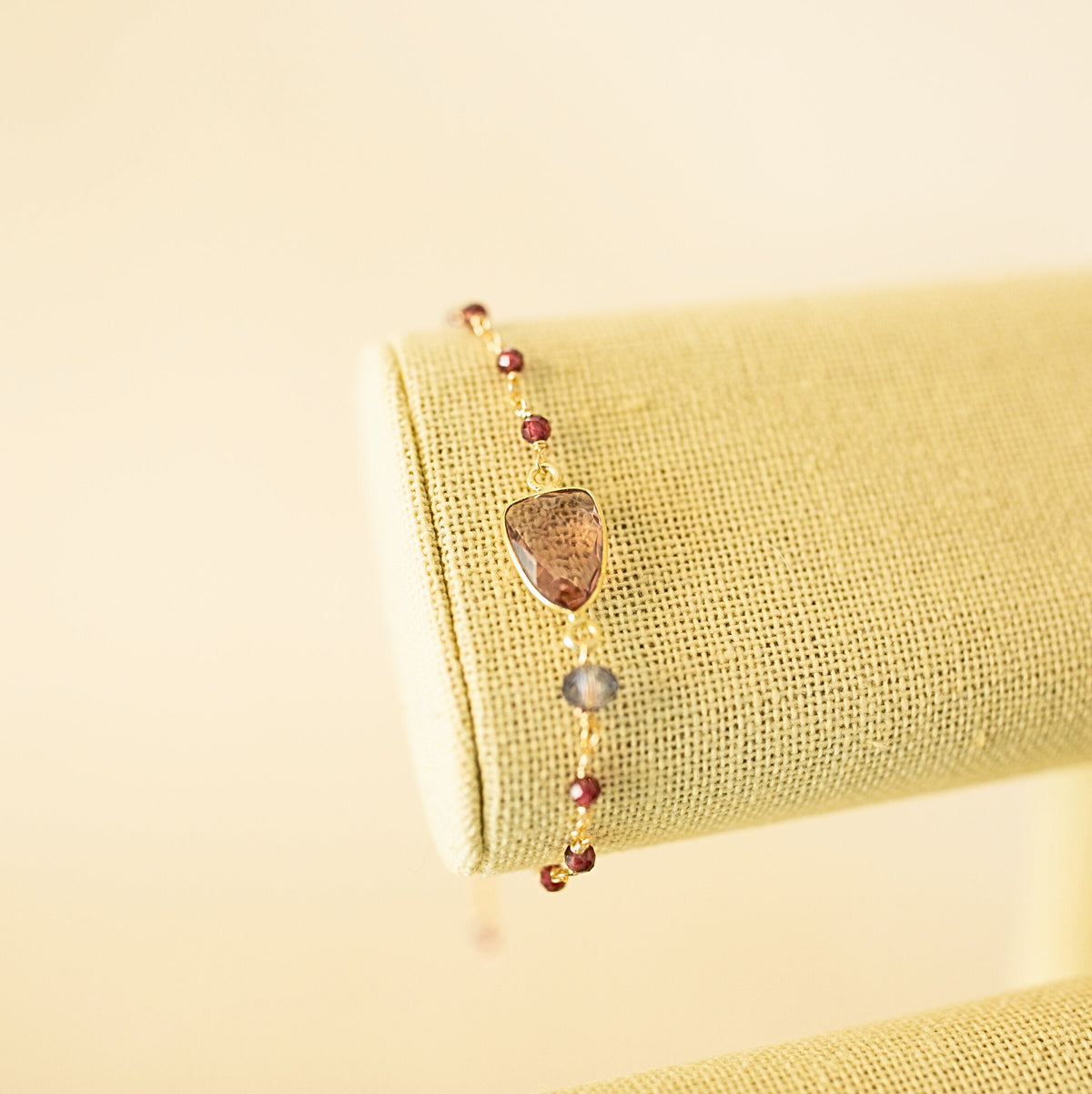 Pink gemstone Isla bracelet with gold-tone links on a fabric display.