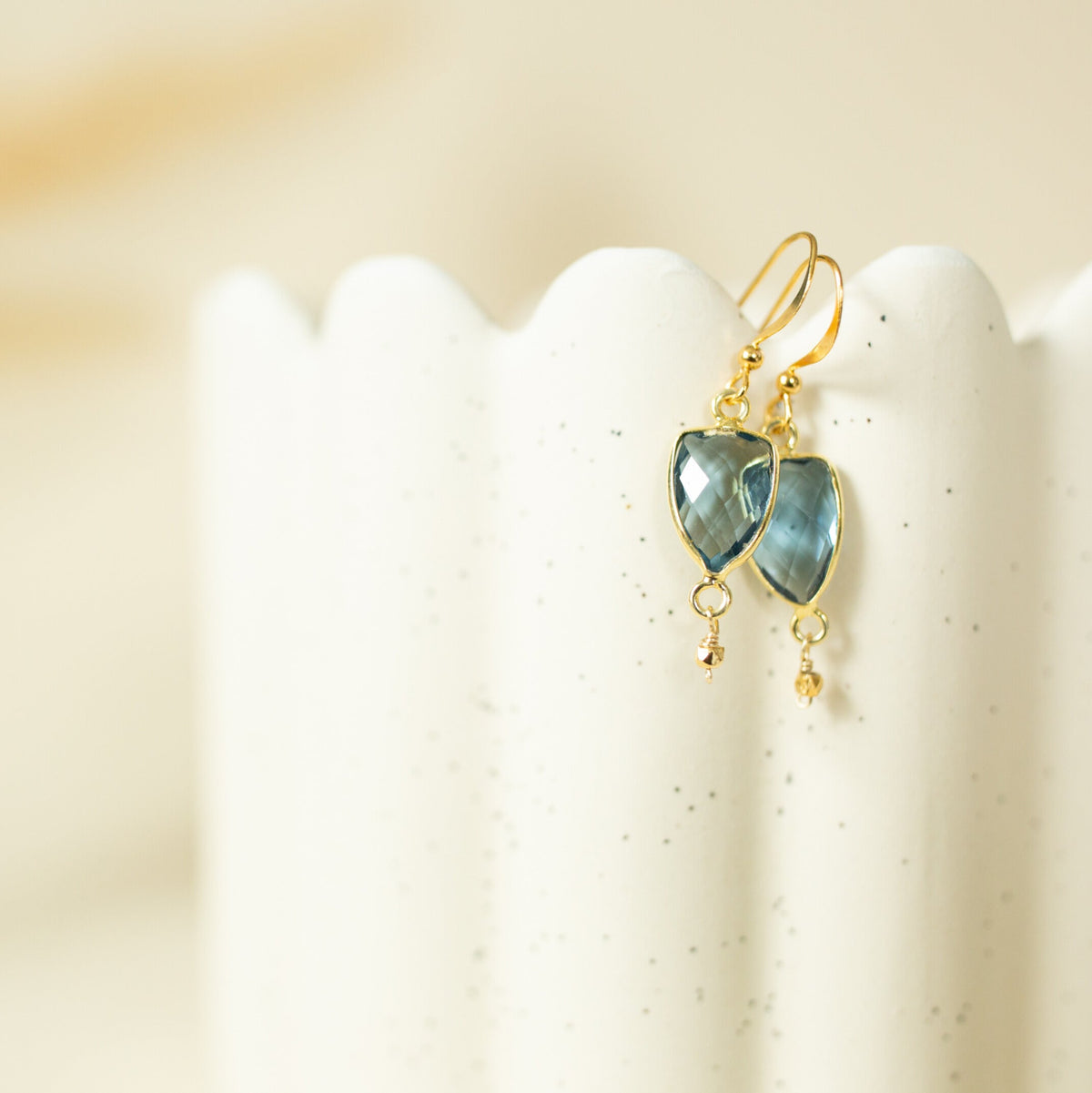 Isla Drops with blue faceted gemstones and gold-tone hooks on a cream display.