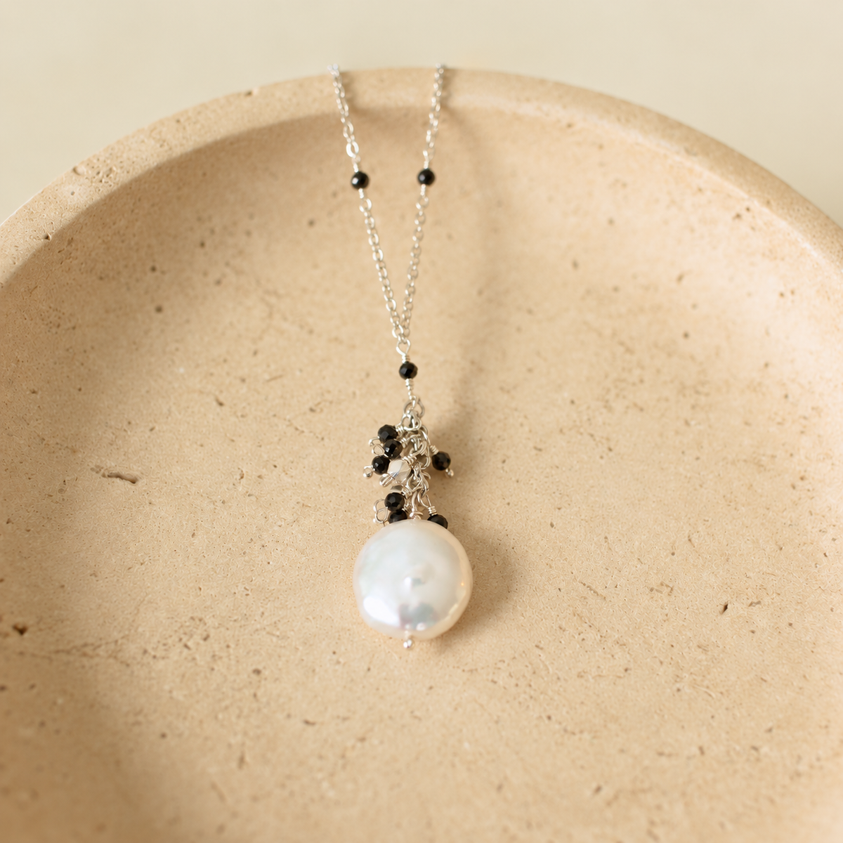 Marea Pendant with Black Spinel, rhodium-plated silver and a freshwater coin pearl on an ivory stone dish; AI-edited from the original product photograph.