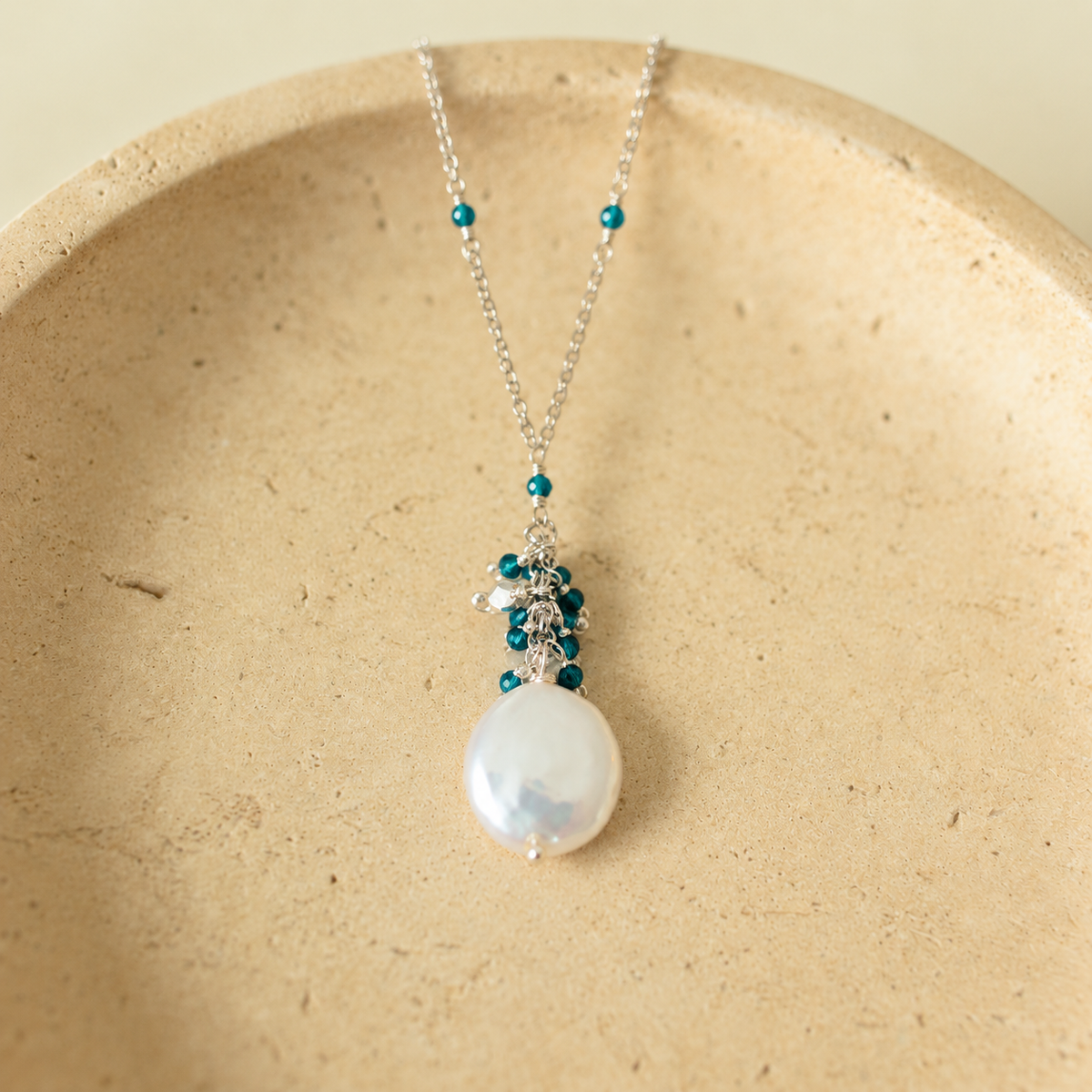 Marea Pendant in London Blue Quartz and rhodium-plated silver, with a freshwater coin pearl on an ivory stone dish; AI-edited from the original product photograph.