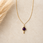 The Amethyst — purple amethyst pendant on a gold-plated silver chain, styled on ivory stone.
