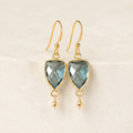 The Isla Drops in London Blue Quartz — refined close-up of faceted stones and gold-plated silver hooks on ivory stone.