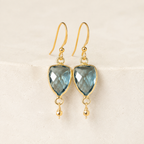 The Isla Drops in London Blue Quartz — refined close-up of faceted stones and gold-plated silver hooks on ivory stone.