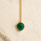 The Onyx green onyx pendant with a fine gold-plated silver chain on warm ivory stone