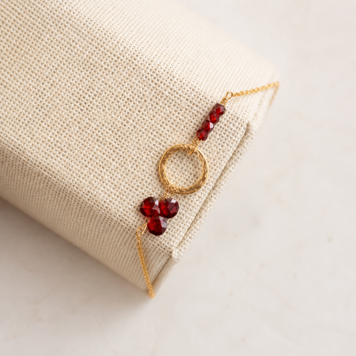 The Solara in Garnet — red faceted beads and a textured gold-plated silver circle on ivory linen.