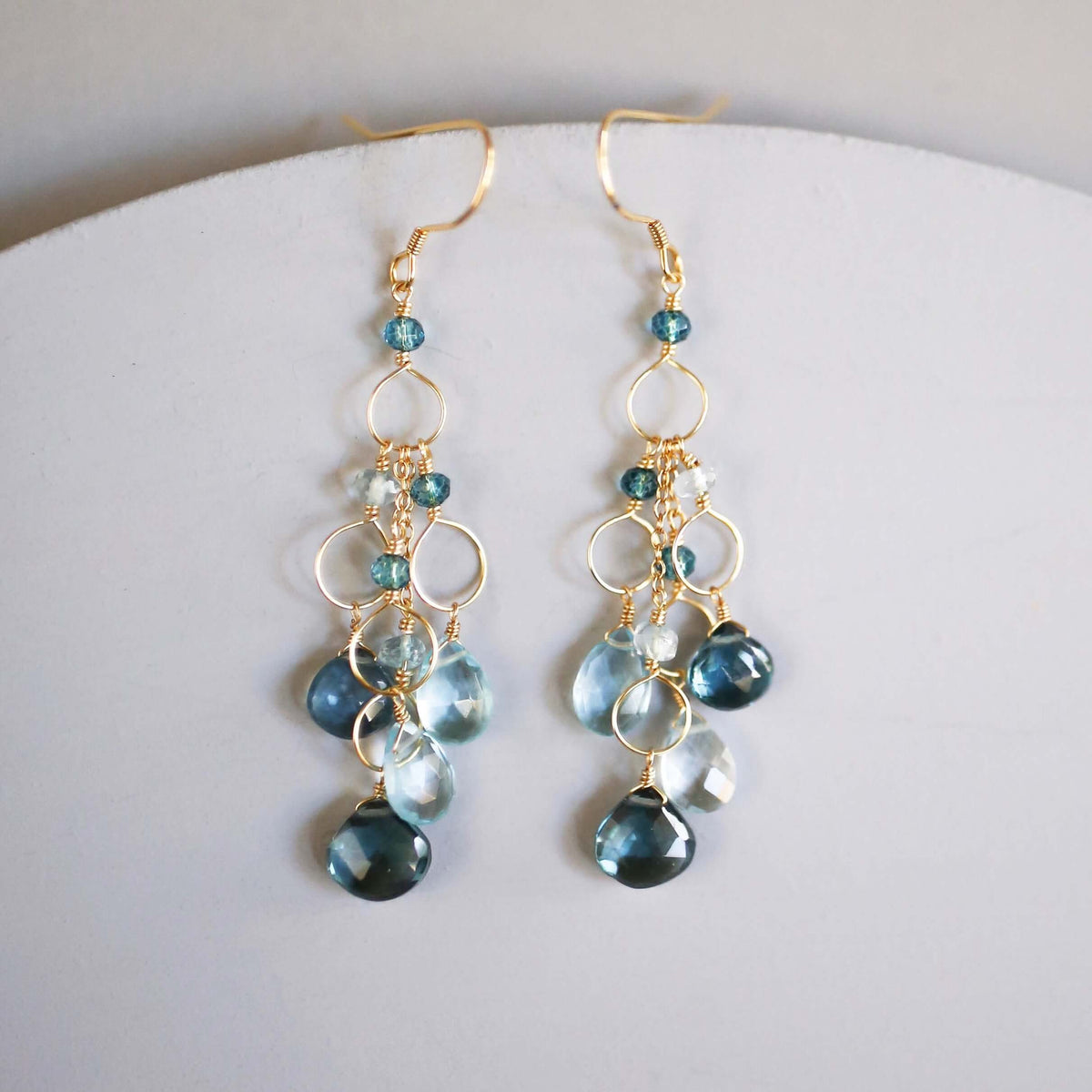 The Cascade Drops in gold, showing the pair of blue gemstone earrings in detail.