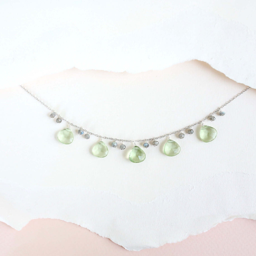 The Prasiolite Necklace with pale green gemstone drops and silver-tone chain, shown against pale paper.