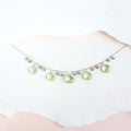 The Prasiolite Necklace with pale green gemstone drops and silver-tone chain, shown against pale paper.