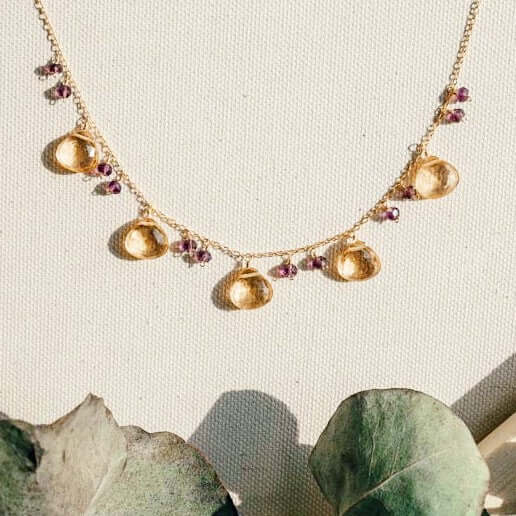 The Citrine Necklace with five golden gemstone drops and small purple bead accents on a fine gold chain.