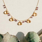 The Citrine Necklace with five golden gemstone drops and small purple bead accents on a fine gold chain.