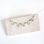 The Prasiolite Necklace with pale green gemstone drops and silver-tone chain, shown on a stone display.